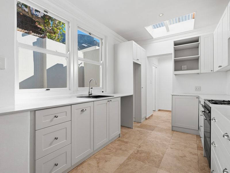 A bright, modern kitchen featuring white cabinetry, stone countertops, a gas hob, and a skylight, finished with neutral tiled flooring.