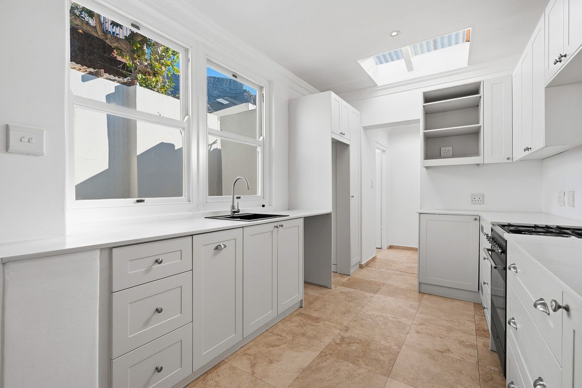 A bright, modern kitchen featuring white cabinetry, stone countertops, a gas hob, and a skylight, finished with neutral tiled flooring.