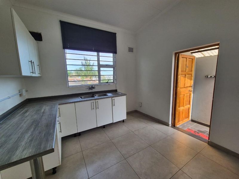 A functional kitchen featuring laminate countertops, built-in cabinetry, and a stainless steel sink, with direct access to an outdoor area.