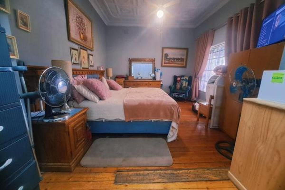 A spacious bedroom featuring original timber flooring, decorative ceiling molding, and a built-in wooden headboard.