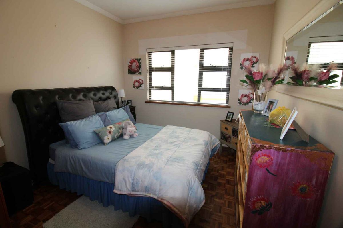 A bedroom featuring parquet flooring, a large window with horizontal blinds, and a wall-mounted mirror.