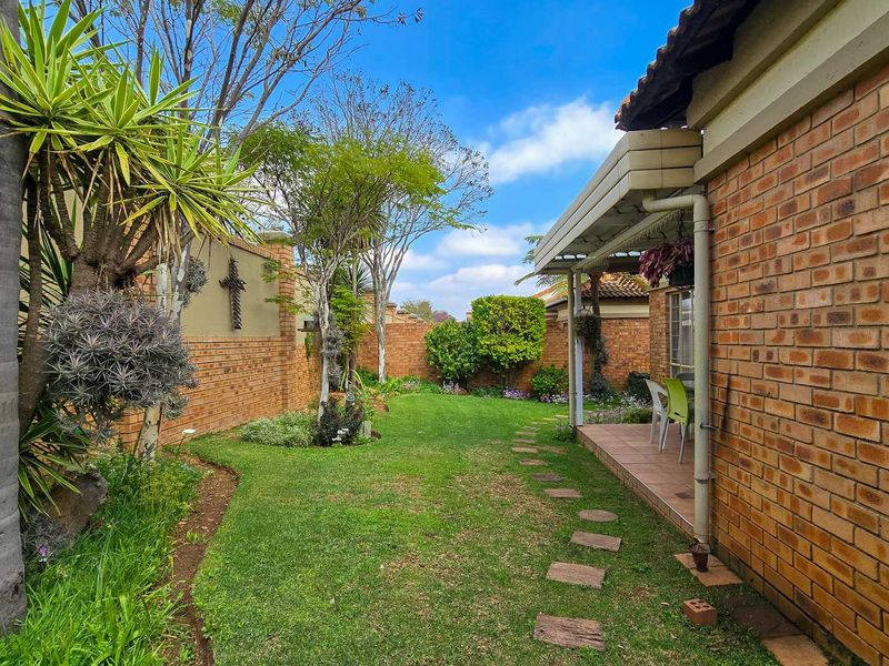 A well-maintained rear garden featuring a brick boundary wall, a covered tiled patio, and a landscaped lawn with a stone pathway.