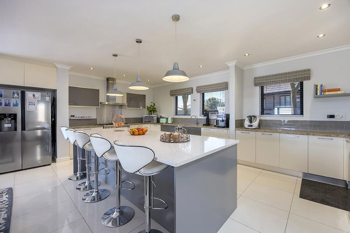 Modern kitchen featuring a large central island with quartz countertops, sleek cabinetry, subway tile backsplash, and high-quality pendant lighting.