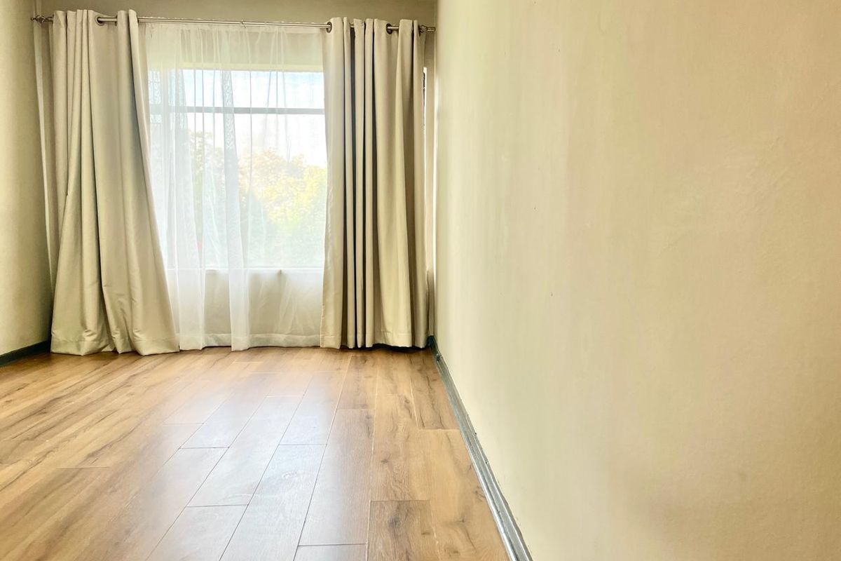 An empty bedroom featuring laminate flooring and a large window with installed curtain rods, offering a blank canvas for personalization.