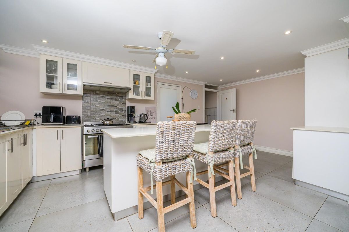 A well-maintained kitchen featuring a central island, stone countertops, tiled flooring, and built-in cabinetry with a gas stove and extractor fan.