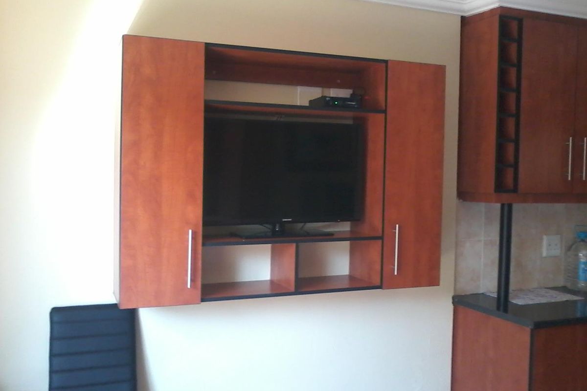 Open plan living area featuring built-in wall cabinetry for media storage and a kitchen section with granite countertops and wooden cabinetry.