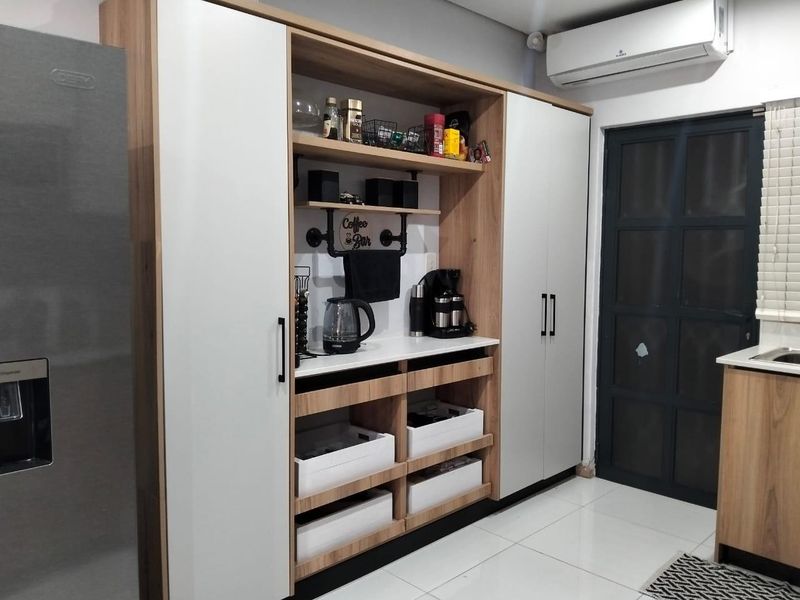 Modern kitchen featuring custom built-in cabinetry with integrated shelving, white countertops, tiled flooring, and a wall-mounted air conditioning unit.