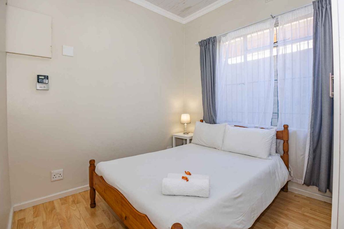 A well-lit bedroom featuring light wood-look flooring, neutral walls, and a window with fitted curtains.