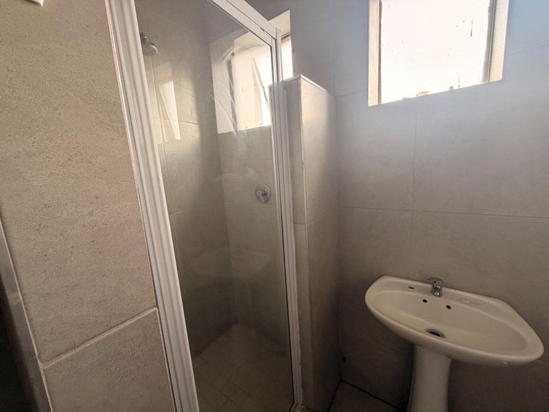 A functional bathroom featuring a tiled shower enclosure and a pedestal basin with neutral wall and floor tiling.