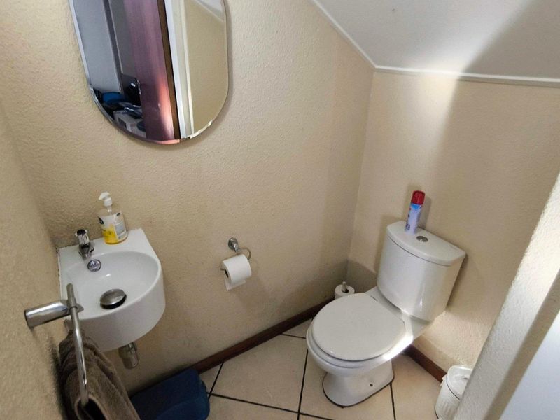 A compact guest bathroom featuring a wall-mounted basin, toilet, and tiled flooring, situated under a sloped ceiling.