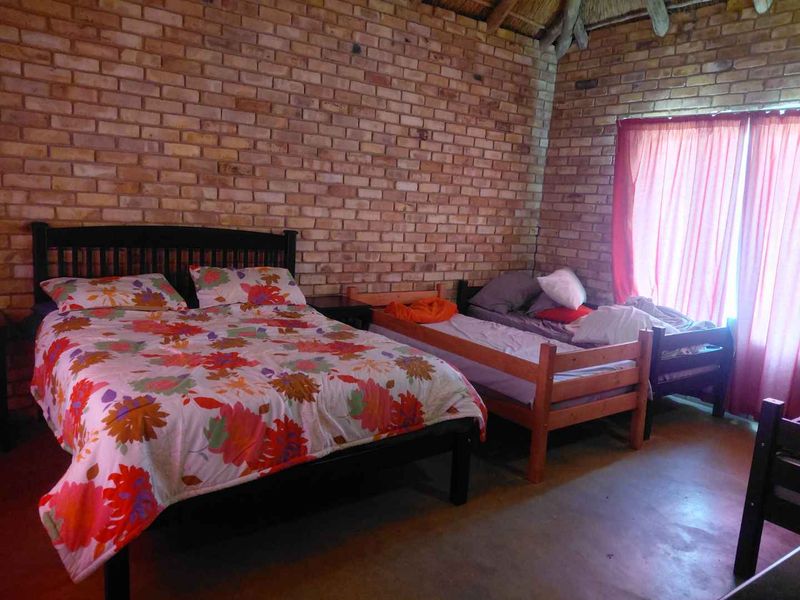 A rustic bedroom featuring exposed brick walls, a traditional thatched roof ceiling, and concrete flooring, offering a cozy and character-filled living space.