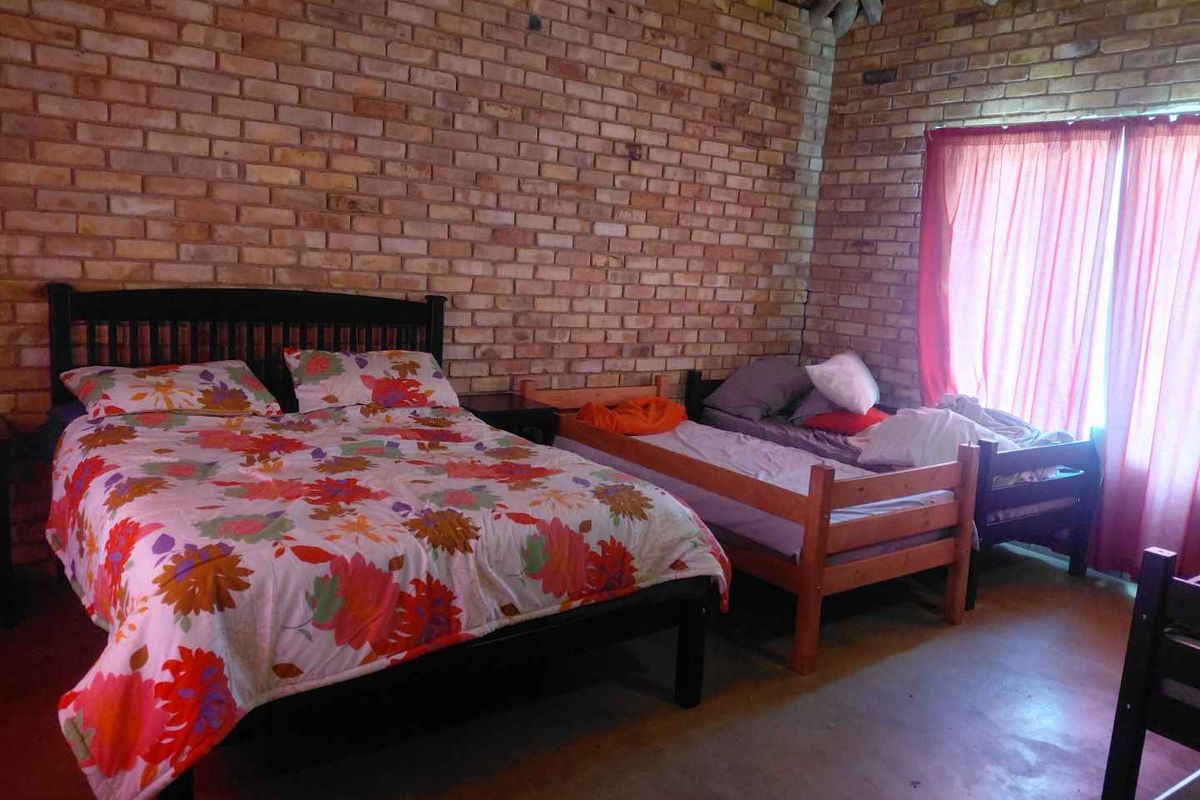 A rustic bedroom featuring exposed brick walls, a traditional thatched roof ceiling, and concrete flooring, offering a cozy and character-filled living space.