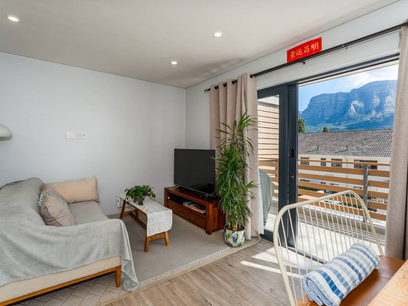 A bright living room featuring laminate flooring, recessed lighting, and a sliding glass door that opens onto a balcony with mountain views.