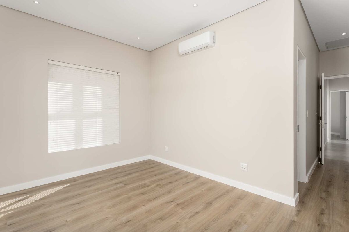 A bright, empty bedroom featuring modern laminate flooring, recessed lighting, and a wall-mounted split-system air conditioner.