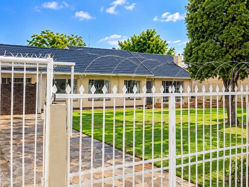 Front view of a single-story house featuring a tiled roof, paved driveway, well-maintained lawn, and secure perimeter fencing with razor wire.