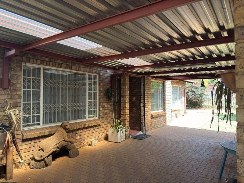 A covered outdoor patio area featuring facebrick walls, paved flooring, and a corrugated metal roof with translucent panels for natural light.