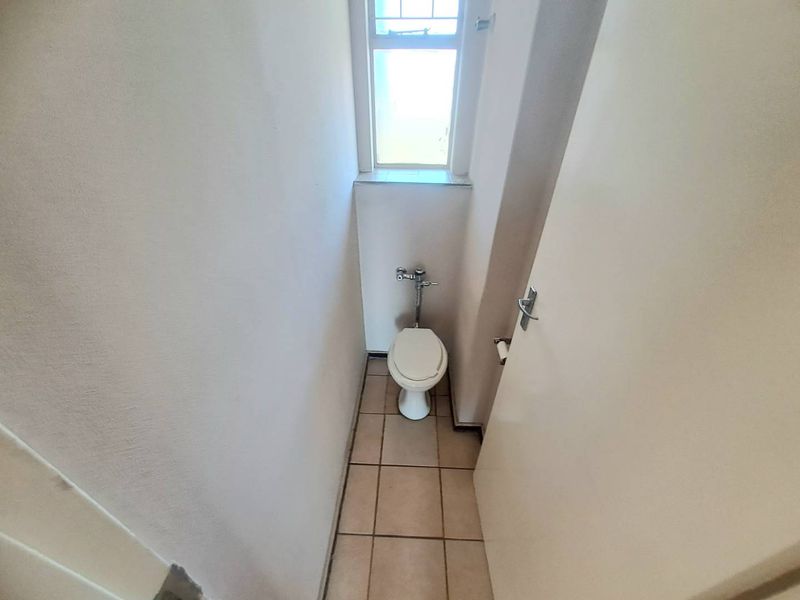 A compact, functional guest toilet featuring ceramic floor tiles and a window for natural light.