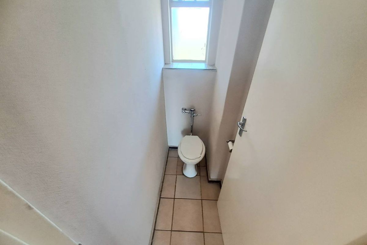 A compact, functional guest toilet featuring ceramic floor tiles and a window for natural light.