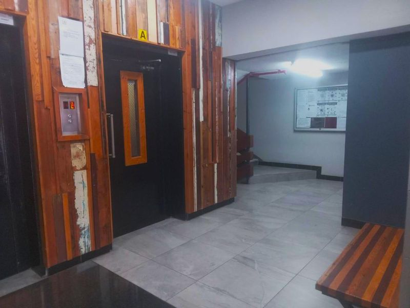Apartment building hallway featuring an elevator, tiled flooring, and decorative wood paneling leading to a communal staircase area.