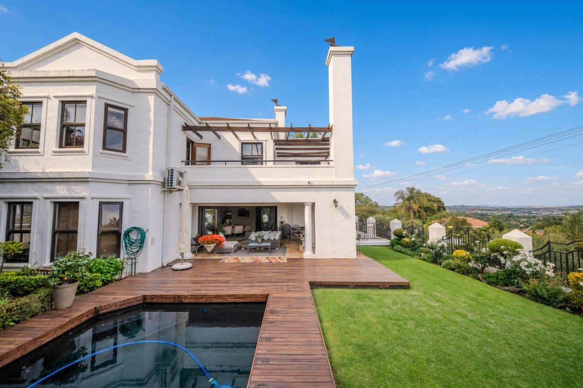 Rear elevation featuring a swimming pool with timber decking, a covered patio, an upper-level balcony, and a well-maintained garden with scenic views.