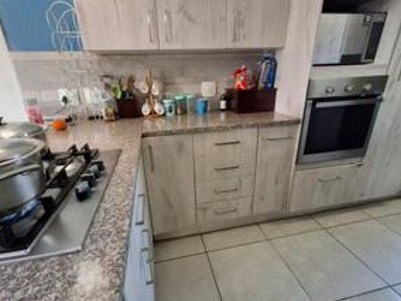 Functional kitchen featuring light wood-grain cabinetry, granite countertops, a gas hob, and integrated oven and microwave appliances with tiled flooring.