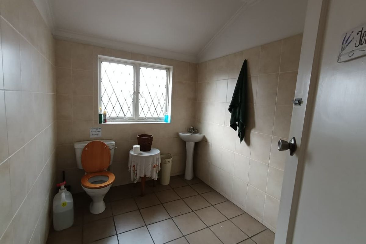 A functional bathroom featuring tiled walls and flooring, a pedestal basin, and a toilet, with a leaded glass window providing natural light.