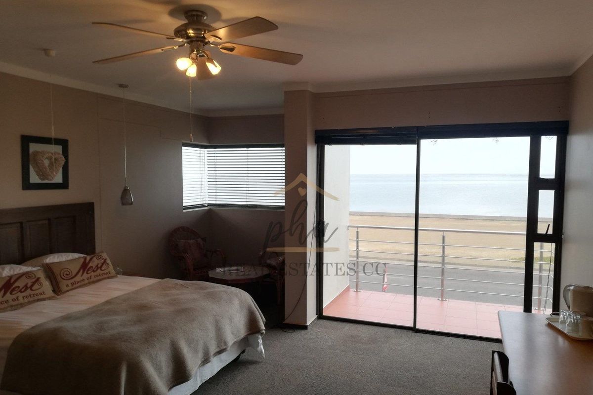 A bedroom featuring a ceiling fan, carpeted flooring, and large sliding glass doors that open onto a balcony with ocean views.