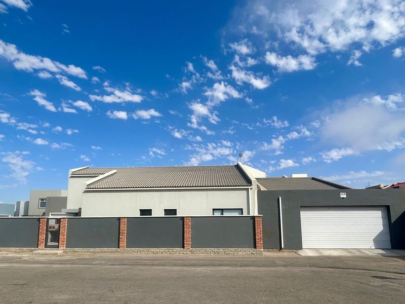 Front elevation of a modern house featuring a tiled roof, secure boundary wall with brick pillars, and a single garage door.