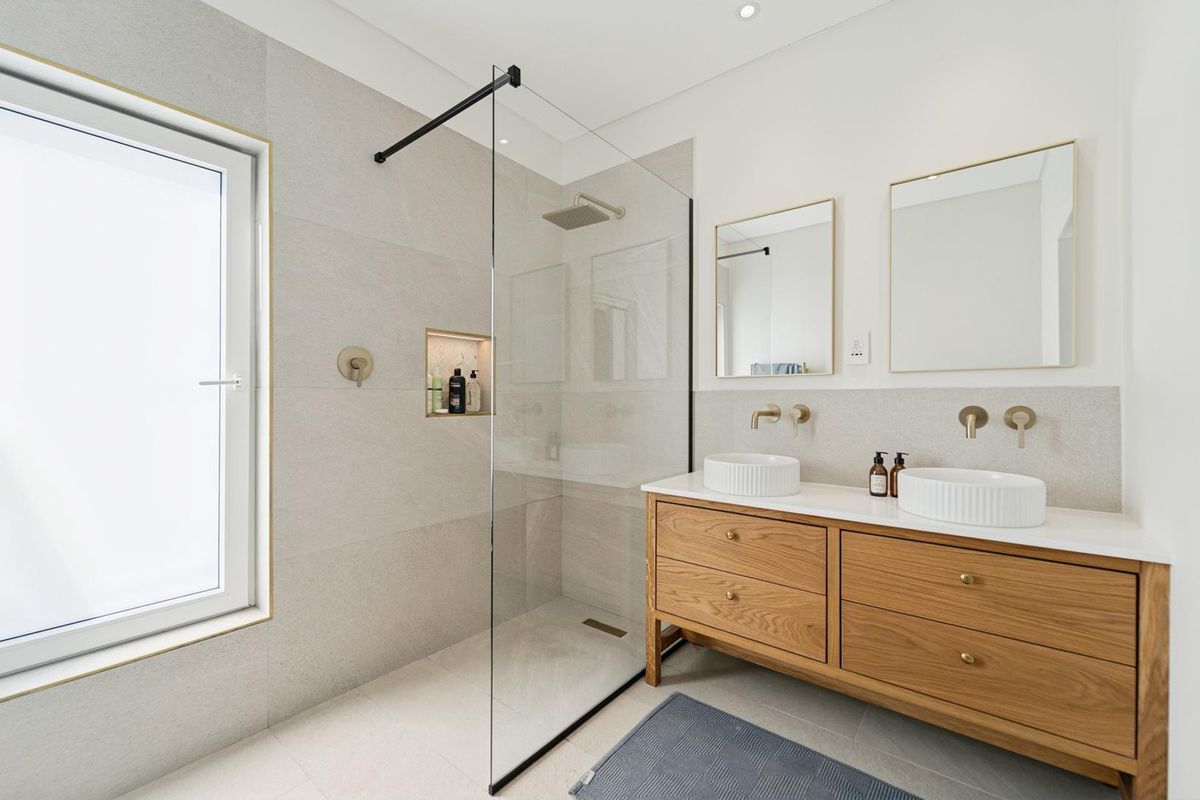 Modern bathroom featuring a double vanity with vessel sinks, a walk-in shower with a glass screen, and contemporary brass fixtures.