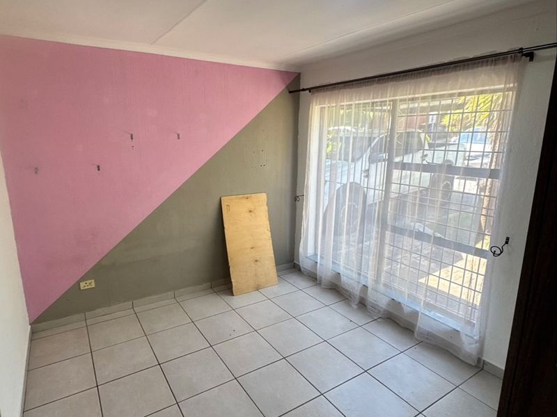 An empty bedroom featuring tiled flooring, a security gate on the window, and a ceiling light fixture, requiring cosmetic updates to the wall finishes.