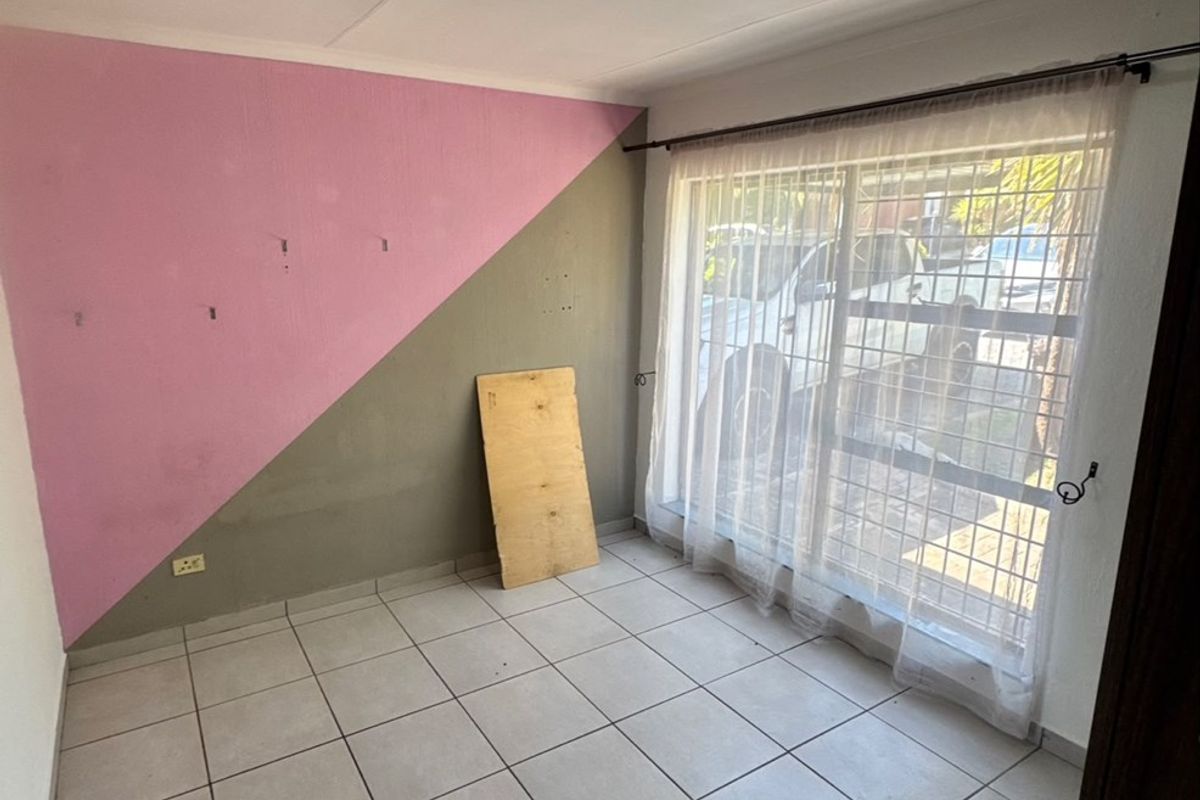 An empty bedroom featuring tiled flooring, a security gate on the window, and a ceiling light fixture, requiring cosmetic updates to the wall finishes.