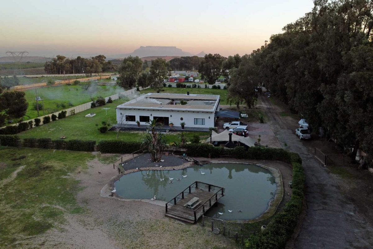 Aerial view of a small holding property featuring a central courtyard-style dwelling, a large garden, and a private pond with a wooden jetty.