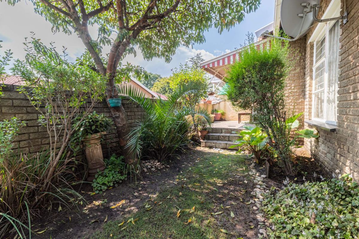 A private rear garden featuring established trees, brick boundary walls, and a paved patio area with a retractable awning.