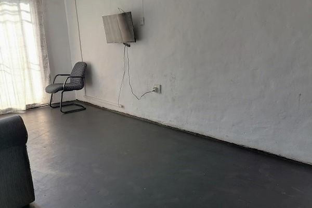 A sparsely furnished living area featuring painted concrete flooring, a sliding glass door, and wall-mounted electrical fixtures.