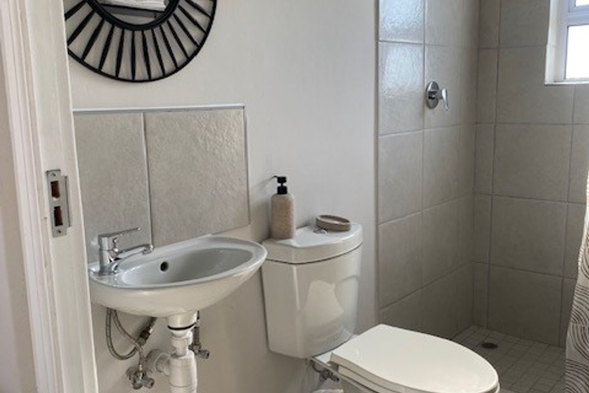 A compact bathroom featuring a wall-mounted basin, a standard toilet, and a tiled shower enclosure with a shower head.