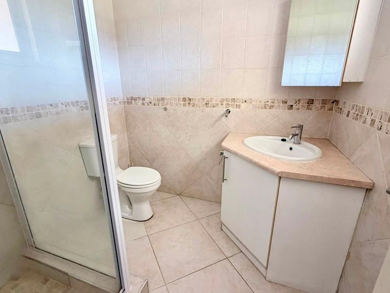 A functional bathroom featuring a corner vanity, a glass-enclosed shower, and neutral wall and floor tiling.