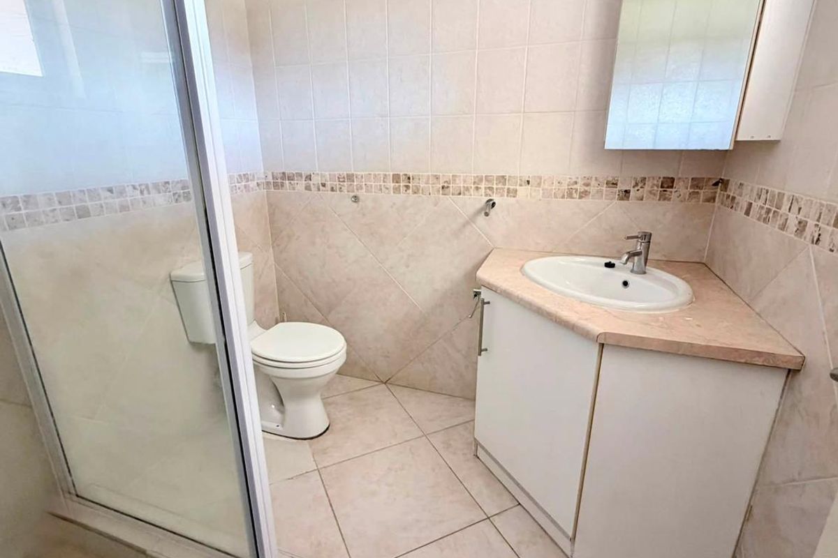 A functional bathroom featuring a corner vanity, a glass-enclosed shower, and neutral wall and floor tiling.