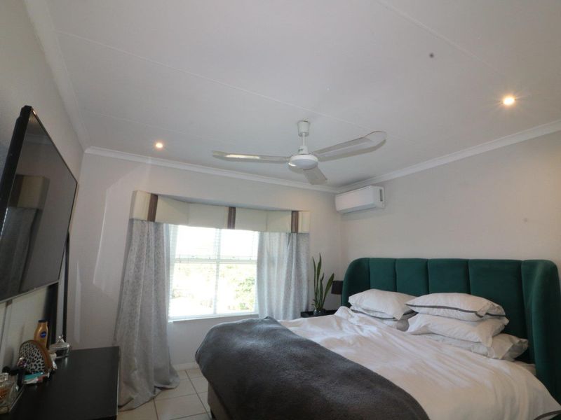 A well-maintained bedroom featuring tiled flooring, a ceiling fan, and a wall-mounted split-system air conditioner for climate control.
