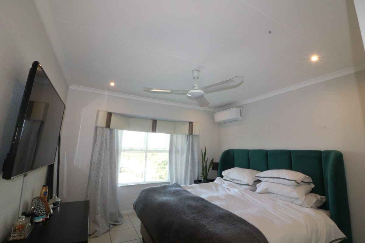 A well-maintained bedroom featuring tiled flooring, a ceiling fan, and a wall-mounted split-system air conditioner for climate control.