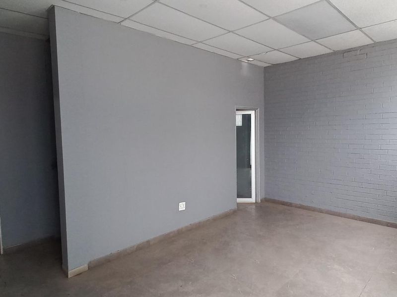 A clean, empty office space featuring painted brick walls, concrete flooring, and a suspended ceiling, providing a versatile industrial workspace.