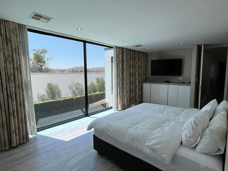 Modern bedroom featuring floor-to-ceiling sliding glass doors, built-in cabinetry, and neutral laminate flooring with access to an outdoor balcony area.