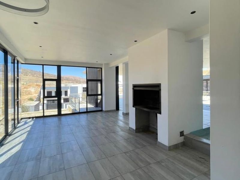 Spacious, modern living area featuring large format floor tiles, a built-in fireplace, and expansive floor-to-ceiling windows offering abundant natural light.
