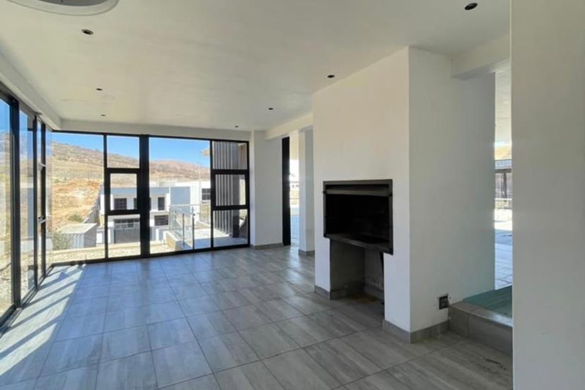 Spacious, modern living area featuring large format floor tiles, a built-in fireplace, and expansive floor-to-ceiling windows offering abundant natural light.