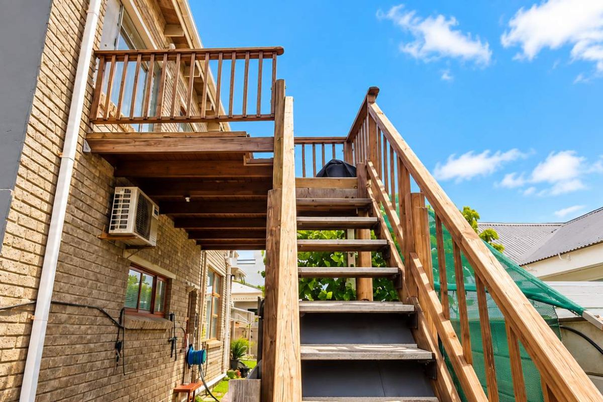 Rear exterior view featuring a wooden staircase leading to an elevated deck, with brick walling and an external air conditioning unit.