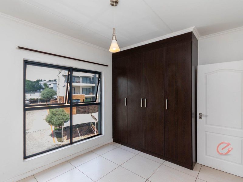 A bright, empty bedroom featuring tiled flooring, a large dark wood built-in wardrobe, and a modern pendant light fixture.