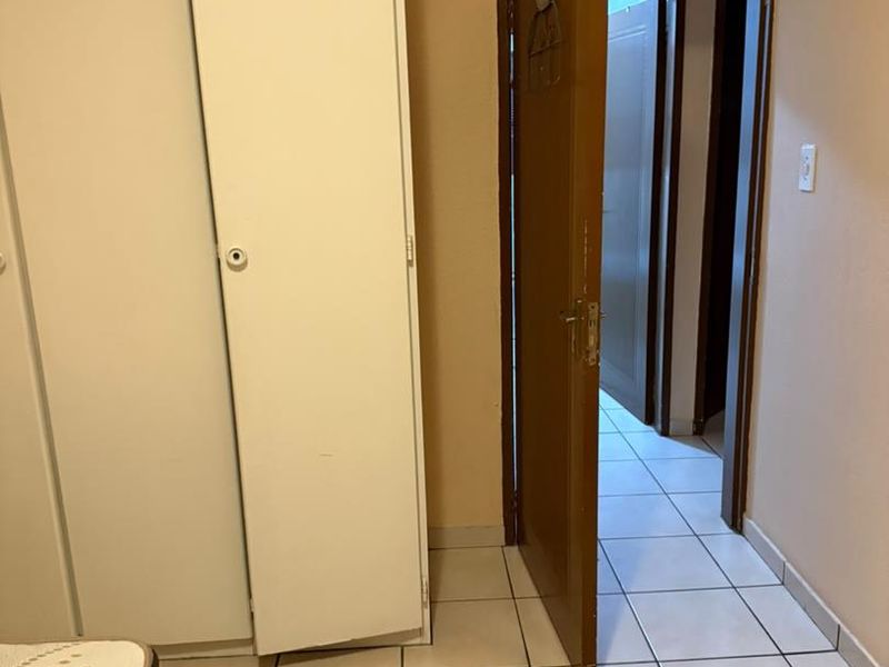 A bedroom featuring tiled flooring and a built-in wardrobe, showing signs of wear on the door frame.