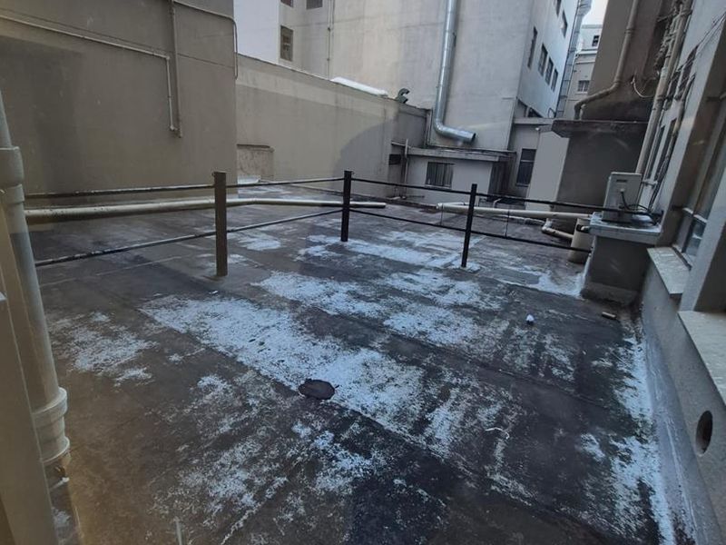 An exterior rear terrace area featuring concrete flooring, metal safety railings, and exposed building drainage infrastructure.