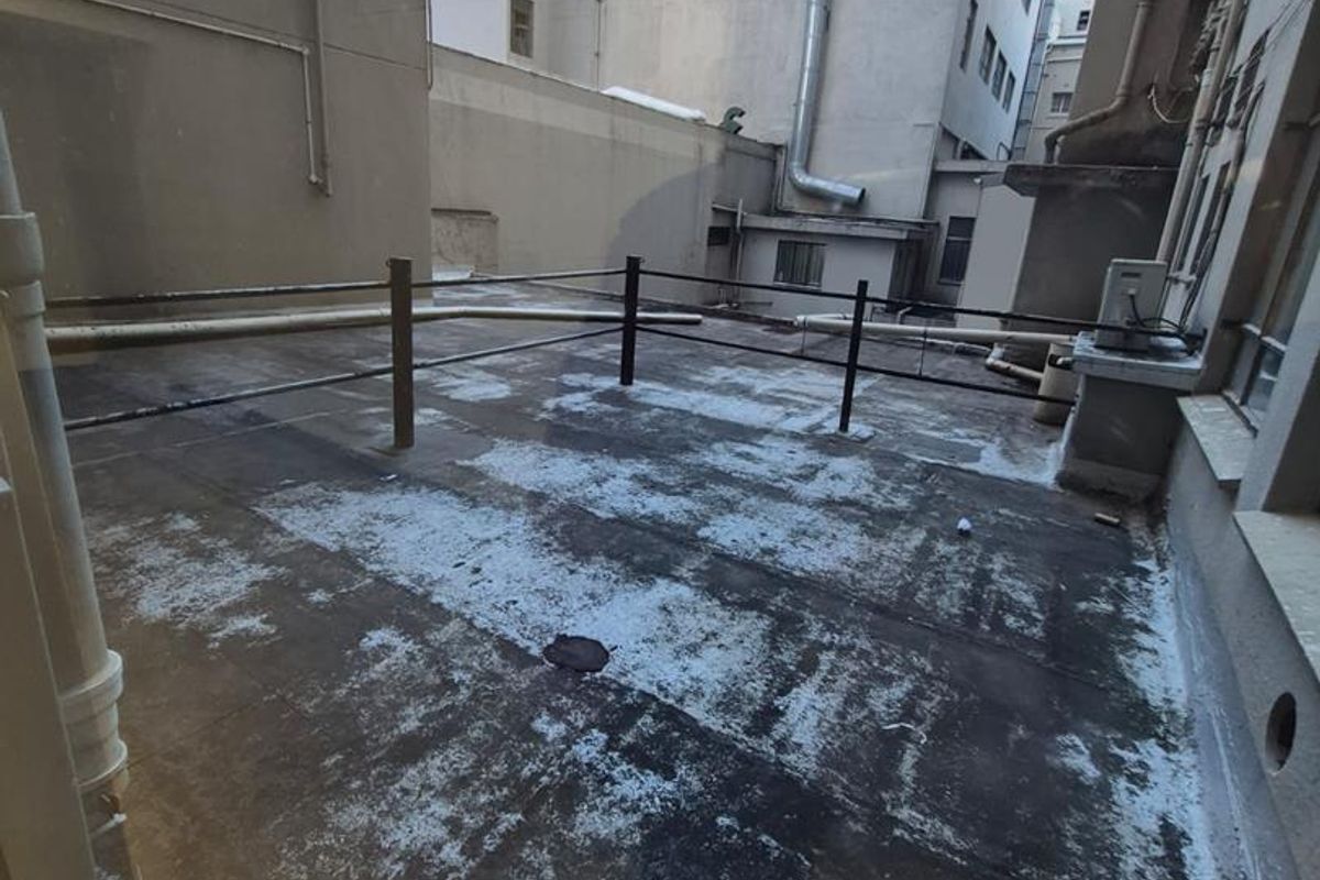 An exterior rear terrace area featuring concrete flooring, metal safety railings, and exposed building drainage infrastructure.
