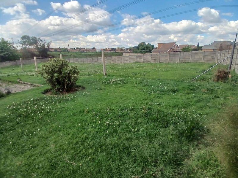 A spacious, level backyard featuring a large grass lawn enclosed by precast concrete walling and concrete fence posts.