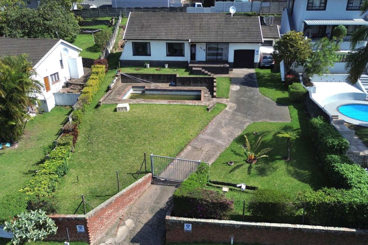 Aerial view of a residential property featuring a large front garden, concrete driveway, garage, and an outdoor swimming pool requiring maintenance.